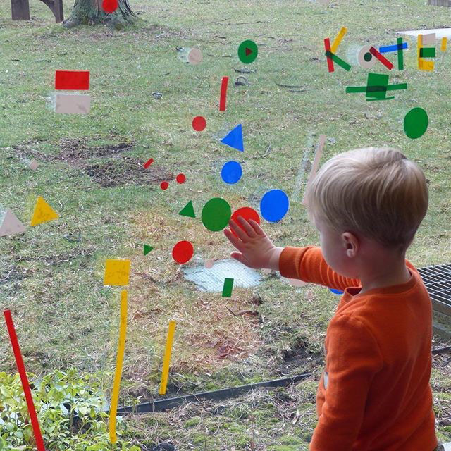 Child placing color-form pieces on glass window